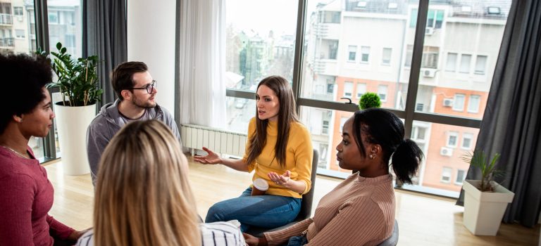 Diverse group of people sitting in circle in group therapy sessi